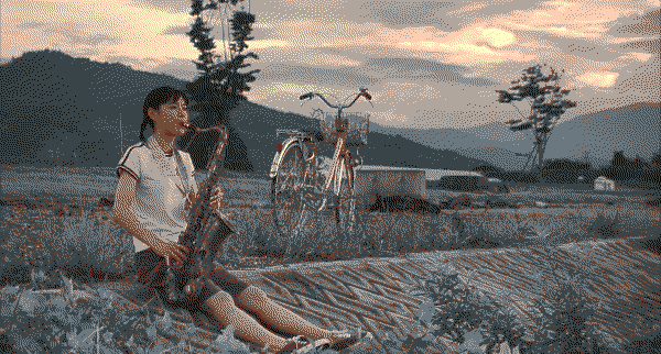 A teenage girl sitting on the ground playing a saxophone