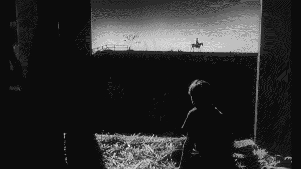 A young boy, sitting in a hayloft, looks out at the silhouette of a man riding a horse along the horizon